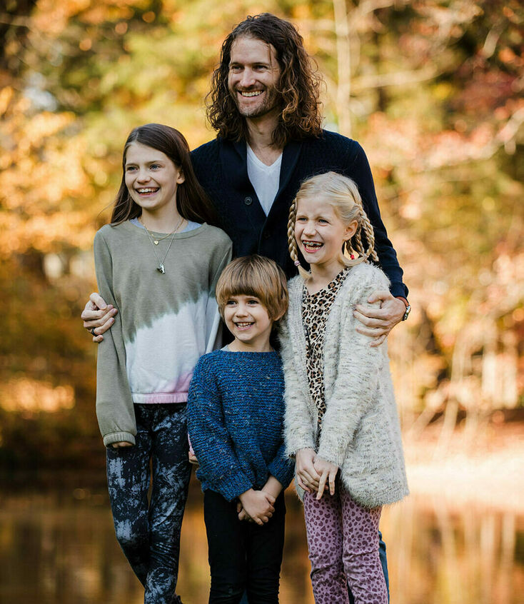 Man, and three kids smiling for a picture with fall foliage in the background