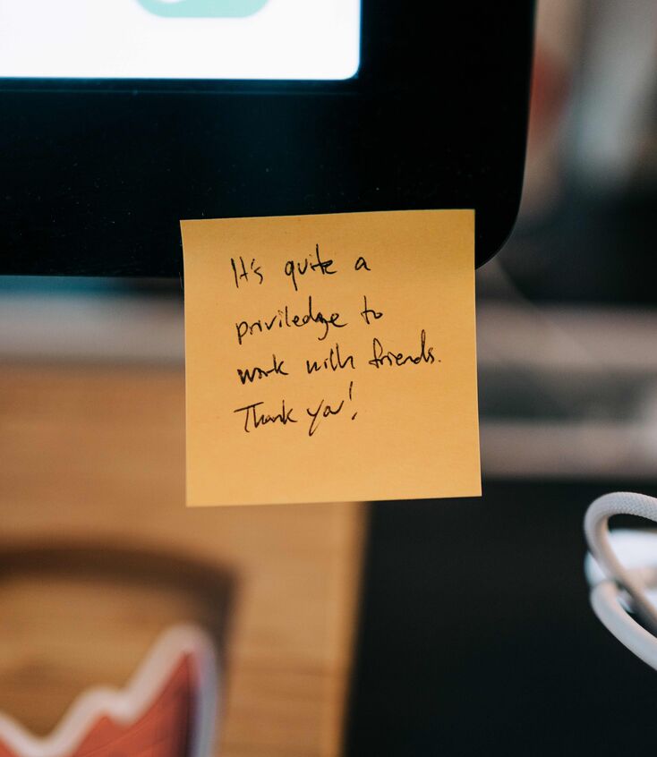 A yellow sticky note on a computer reading "it is quite a privilege to work with friends. Thank you!