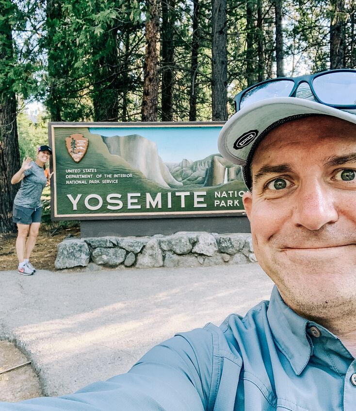 Mighty team member in front of the Yosemite National Park sign with a button up shirt and hat on.